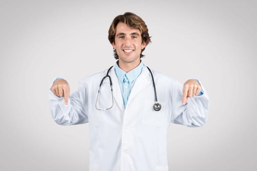Happy male doctor pointing downwards with both hands