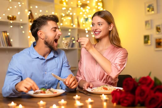 Woman feeding man pasta at romantic candlelit dinner