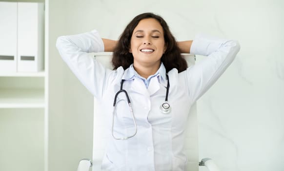Calm young woman doctor reclining on chair at office