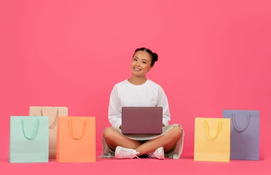 Internet Purchases. Asian Woman Sitting On Floor With Laptop And Shopping Bags