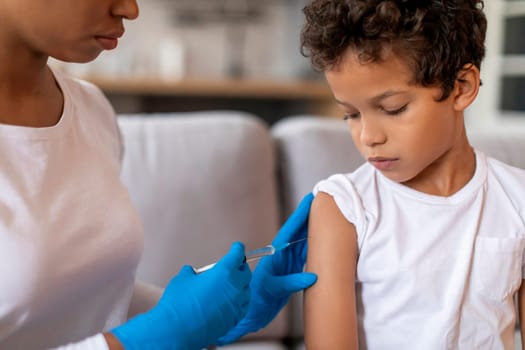 Doctor making vaccination against flu for little black boy in home interior