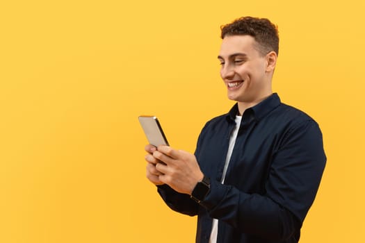 Positive guy using smartphone on yellow background