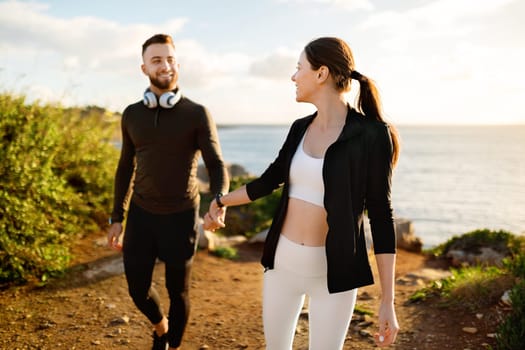 Couple holding hands and smiling on seaside walk after workout