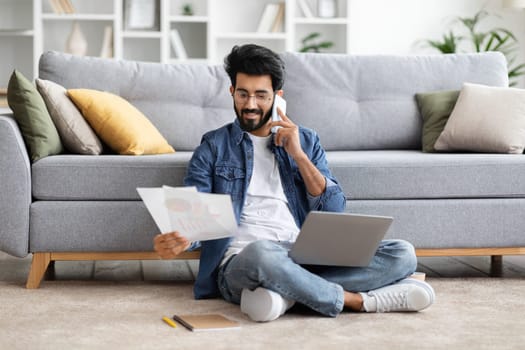 Focused indian man working from home, talking on phone and analyzing documents
