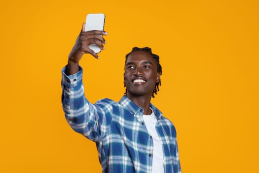 Cheerful young black man taking selfie with smartphone