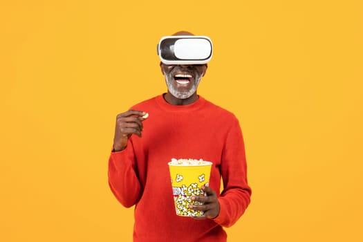 Smiling inspired senior african american man in vr 3d glasses, eat popcorn, watch film