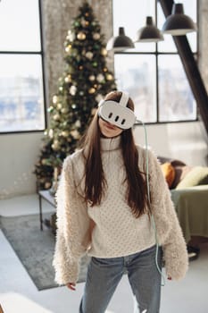 Immersed in virtual reality, a beautiful young woman stands beside a Christmas tree.