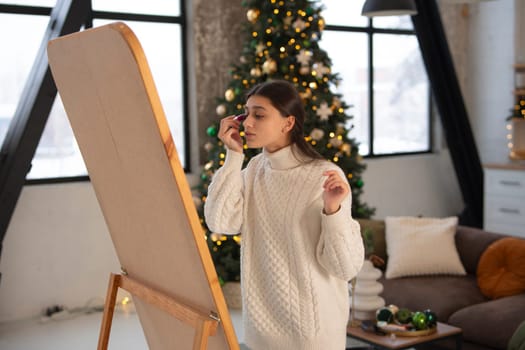 Creating a festive mood, a beautiful young woman does makeup in a Christmas setting.