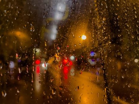 Rain bokeh road lights. Abstract shot of evening city traffic bokeh. Multicolored lights of the evening city and passing cars through a wet rainy window.