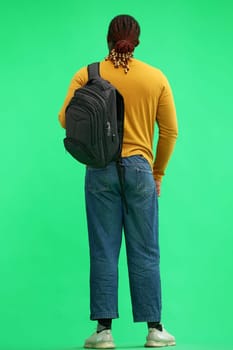 man in a yellow sweater with a backpack on a green background, back view