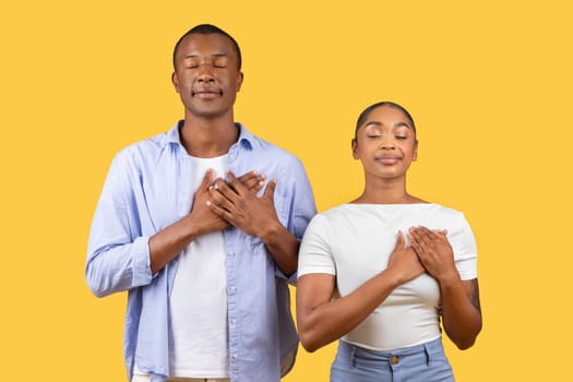 Grateful couple with hands on hearts, eyes closed, yellow background