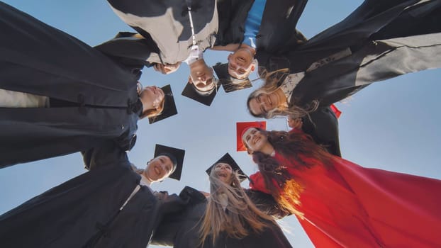 College graduates in a circle stand hugging each other.