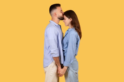 Loving couple forehead kiss, eyes closed on yellow background