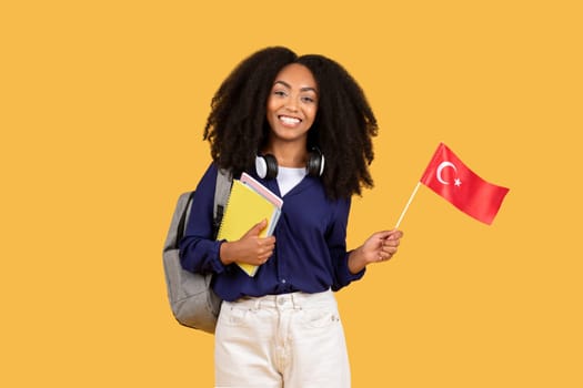 Excited black student with Turkish flag and notebooks on yellow background
