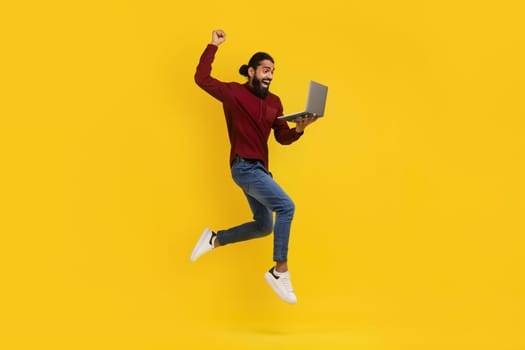 Excited eastern man jumping up with laptop in his hand