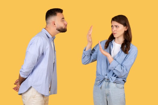 Man trying to kiss woman who shows stop gesture on yellow background