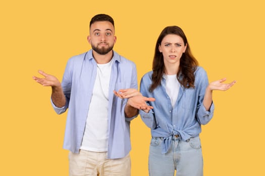 Confused couple shrugging, uncertain expressions, yellow backdrop