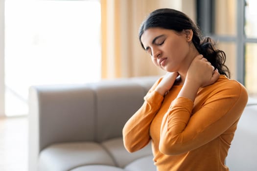 Tired Indian Woman Suffering Neck Pain While Sitting On Couch At Home