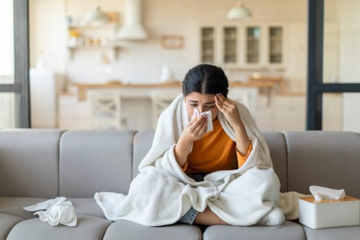 Ill indian woman blowing her nose with tissue at home