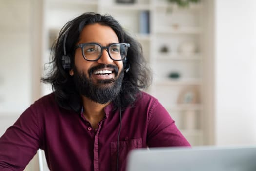 Indian freelancer guy with glasses and headset sitting at desk with laptop
