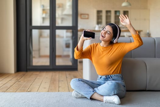 Joyful woman dancing and singing with smartphone at home