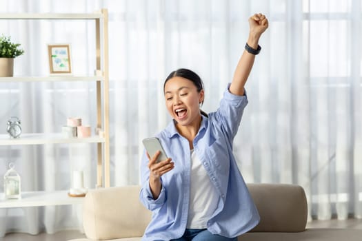 Emotional asian woman looking at smartphone screen and gesturing