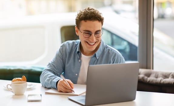Smiling millennial european guy in glasses, typing on laptop, work, study or online communication