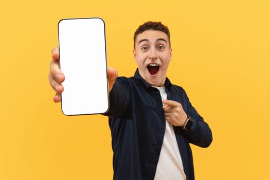 Amazed young guy showing phone with white blank screen