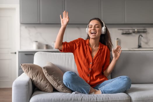 Joyful woman with headphones singing at home on sofa