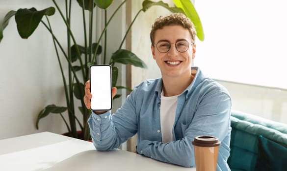Cheerful millennial european guy in glasses show smartphone with empty screen