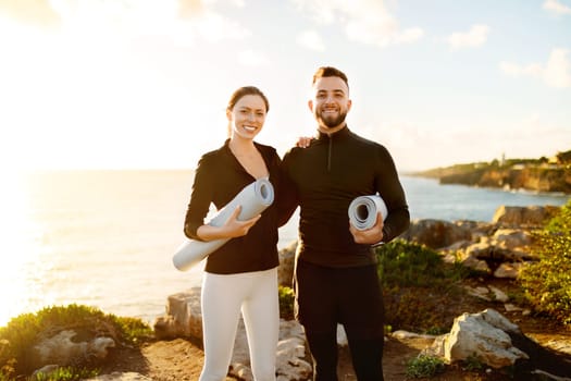 Fit happy couple with yoga mats ready for seaside workout