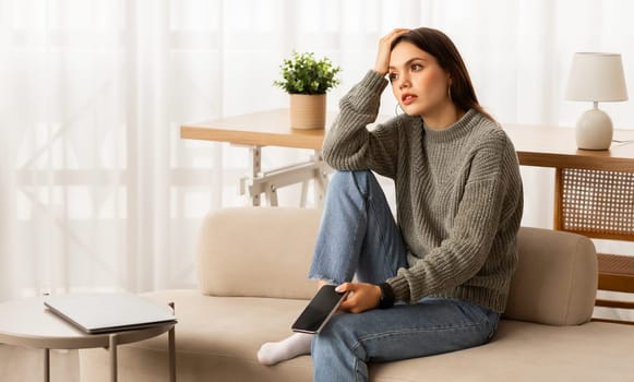 Upset young woman sitting at home, waiting for call
