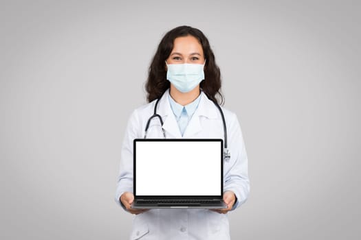 Doctor woman with mask presenting white laptop screen