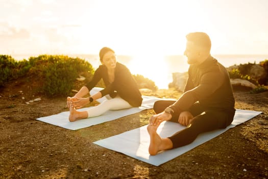 Couple sharing laugh while doing yoga stretches seaside