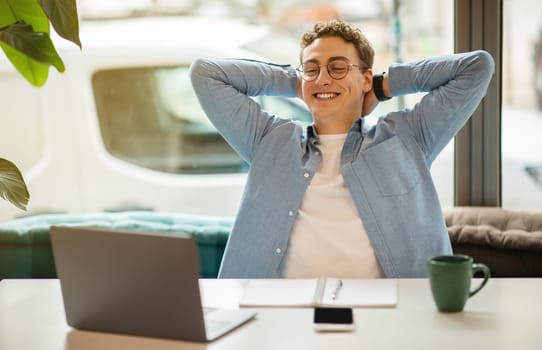 Cheerful young european man student in glasses, look at laptop, rest from work