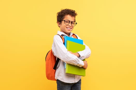Confident black student teen with glasses and backpack on yellow
