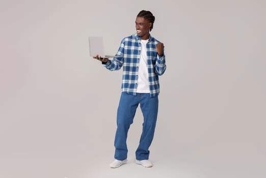 Portrait Of Joyful Black Man Celebrating Success With Laptop, Raising Clenched Fist