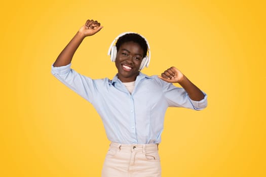 Glad african american young woman student with headphones dance, enjoy music