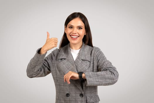 Joyful woman giving thumbs up with smartwatch