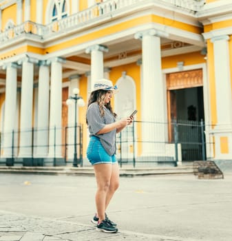 Lifestyle of tourist girl texting with phone on the street of square. Beautiful young travel girl with hat using cell phone on the street of Granada Nicaragua