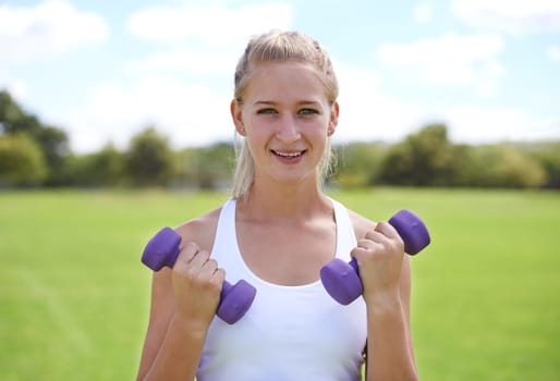 Woman, portrait and dumbbells outdoor for workout with smile for exercise, training or fitness on sports field. Athlete, person and happy for physical activity or healthy body on grass with equipment