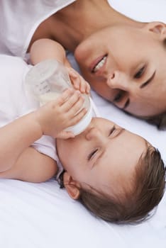 Above, care and a mother with a baby and milk for nutrition, health and growth development. Morning, family and a young mom and child with a bottle in the bedroom of a house for food and a drink