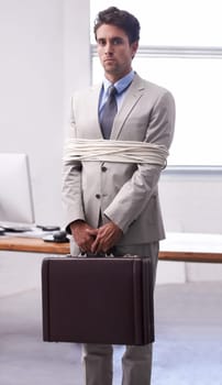 Portrait of businessman in office tied up in rope with depression, control and fear in law firm. Serious attorney, lawyer or legal consultant bound at work, corporate hostage with bag and stress.