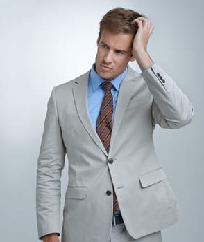 Confused, thinking and young businessman in a studio with doubt, unsure or decision facial expression. Choice, uncertain and professional male person in a suit with question face by gray background.
