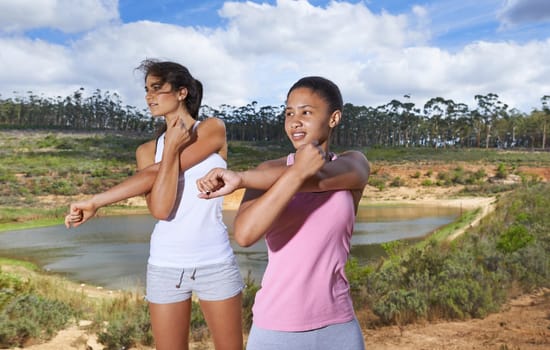 Young women, stretching and fitness in countryside for exercise in outdoor by trees and blue sky. Diversity, teenagers and cardio workout in gym clothes, healthy and wellness with training in forest