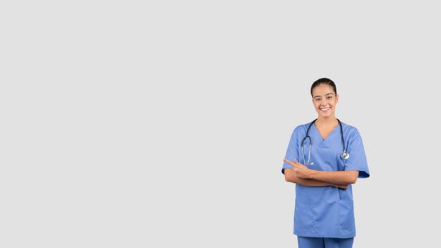 Cheerful european nurse in blue scrubs with crossed arms and a stethoscope