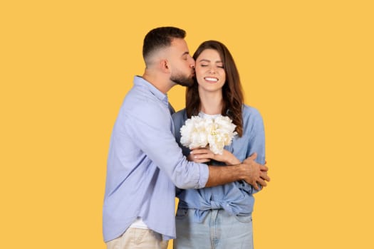 Man kissing woman on cheek, she holds flowers, expressing affection