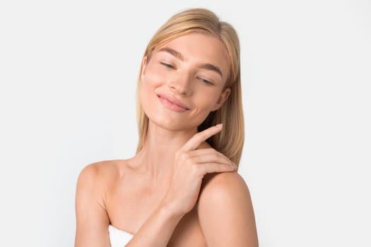 Caucasian blonde woman delicately touching her shoulder over white background