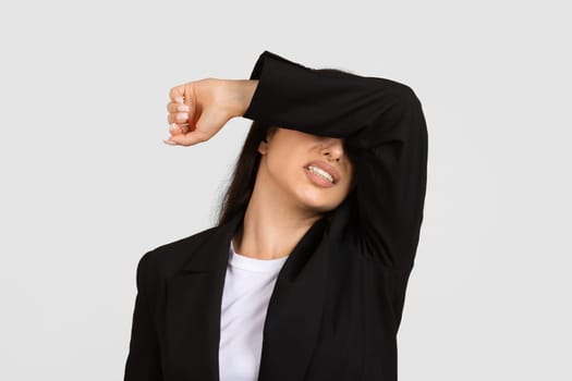 Despaired businesswoman, with pained expression, covering eyes with hand, isolated on gray background