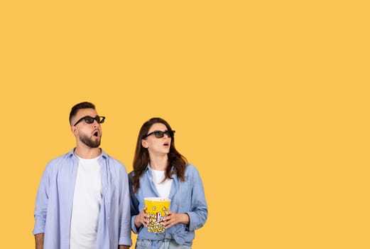 Amazed couple in 3D glasses with popcorn looking up in excitement